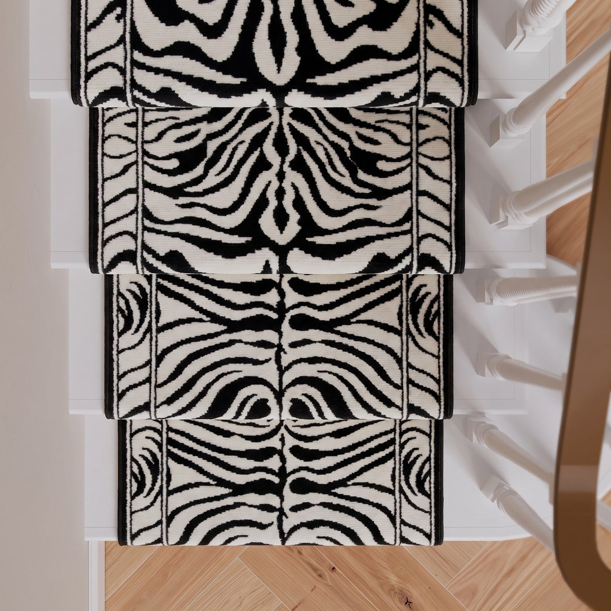Four black and white zebra-print stair runner rugs arranged on a staircase with light wood flooring and white banister posts visible.