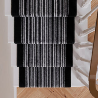Four black stair runner rugs with white and gray vertical stripes, shown installed on a staircase with light wood flooring.