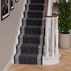 A black and gray patterned carpet stair runner with white Greek key borders, shown installed on a staircase in a home interior.