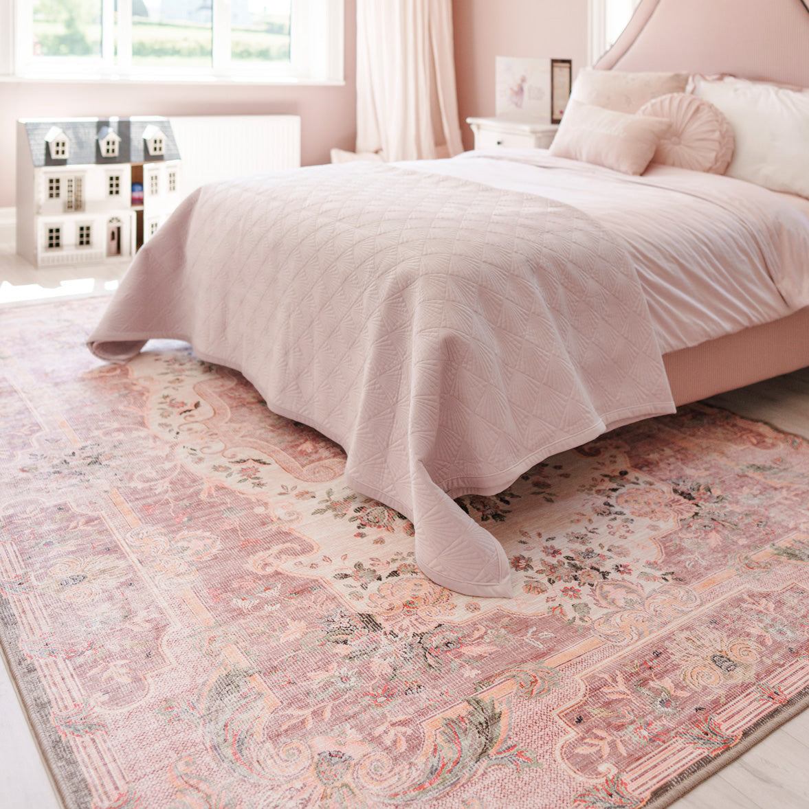 Bedroom with a pink bedspread and patterned rug.