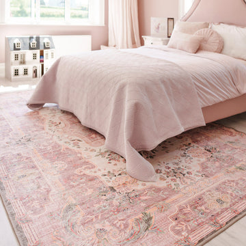 Bedroom with a pink bedspread and patterned rug.