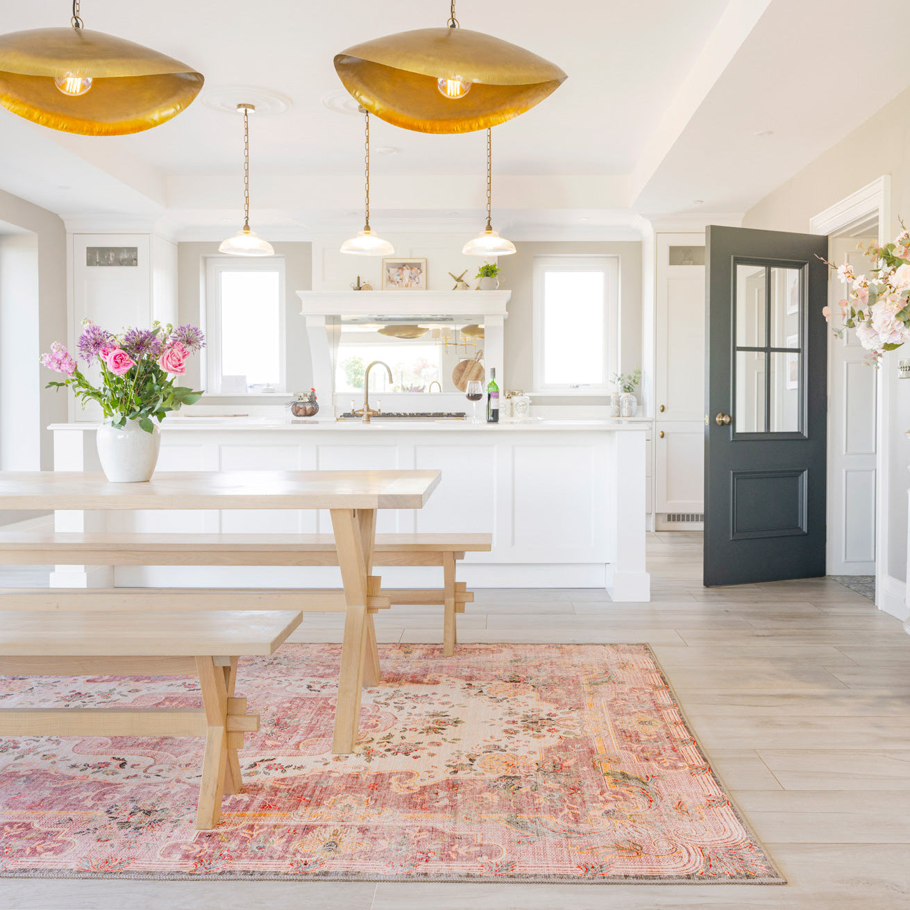 Modern kitchen with white cabinets, wooden dining table, and decorative rug.