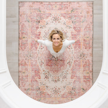 Woman lying on a large floral-patterned rug in a room with wooden flooring.