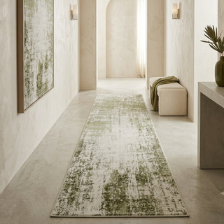 A long runner rug with a distressed green and off-white pattern is displayed in a modern, minimalist hallway with textured beige walls and concrete floors.