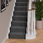 A dark gray and black striped stair runner carpet installed on a staircase with white balusters and a light wood floor.