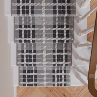 Four gray and black plaid stair runner rugs arranged on a staircase with light wood flooring and white banister posts.