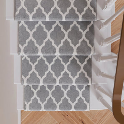 Four gray and white patterned stair runner mats arranged on a staircase with light wood flooring and white banister posts visible.