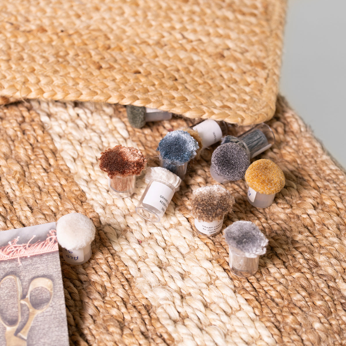 A set of small fabric or rug brush samples with white handles and colorful bristles, arranged on a woven jute rug next to a package card.