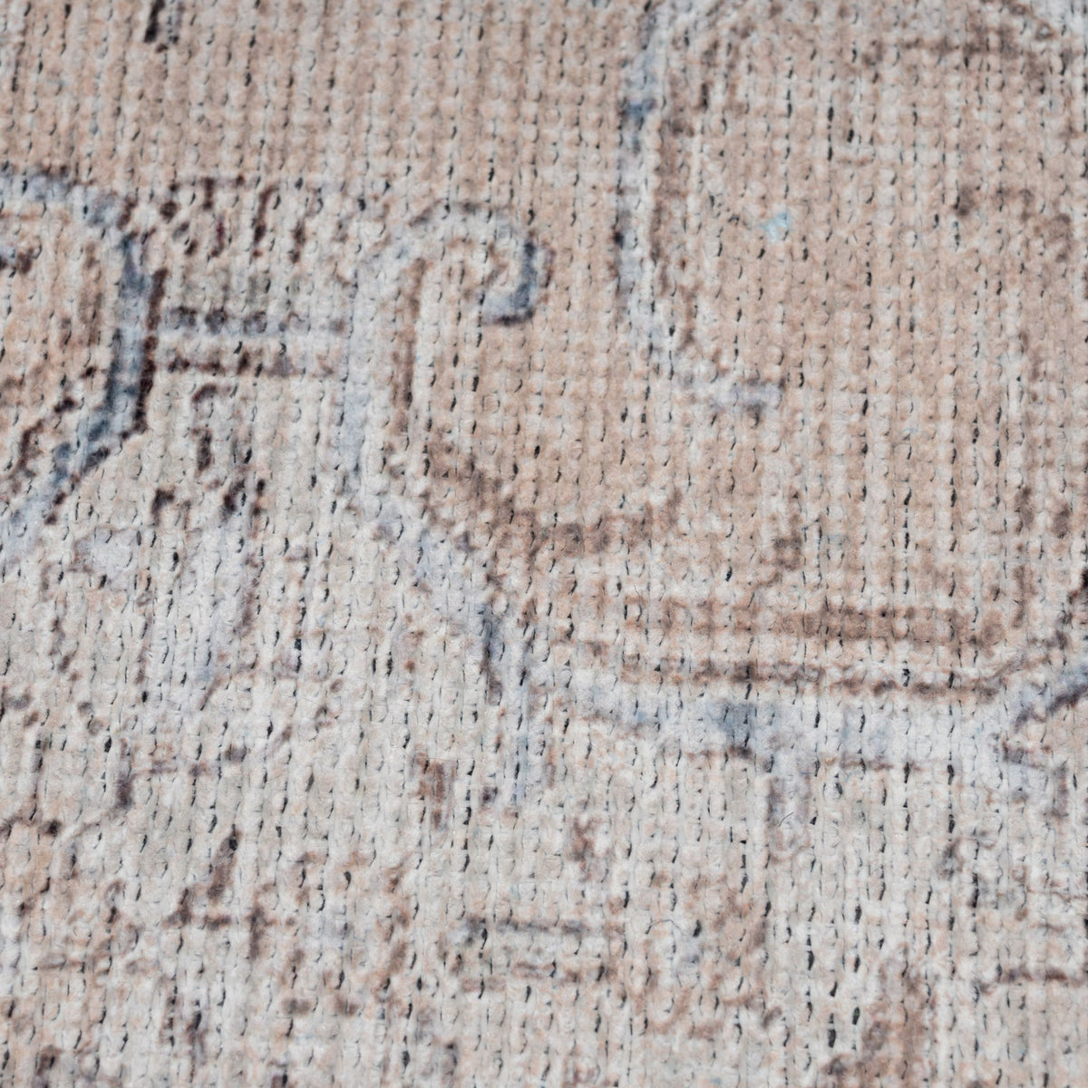 A close-up of a vintage-style area rug with a distressed, faded pattern in beige, taupe, and light blue-gray.