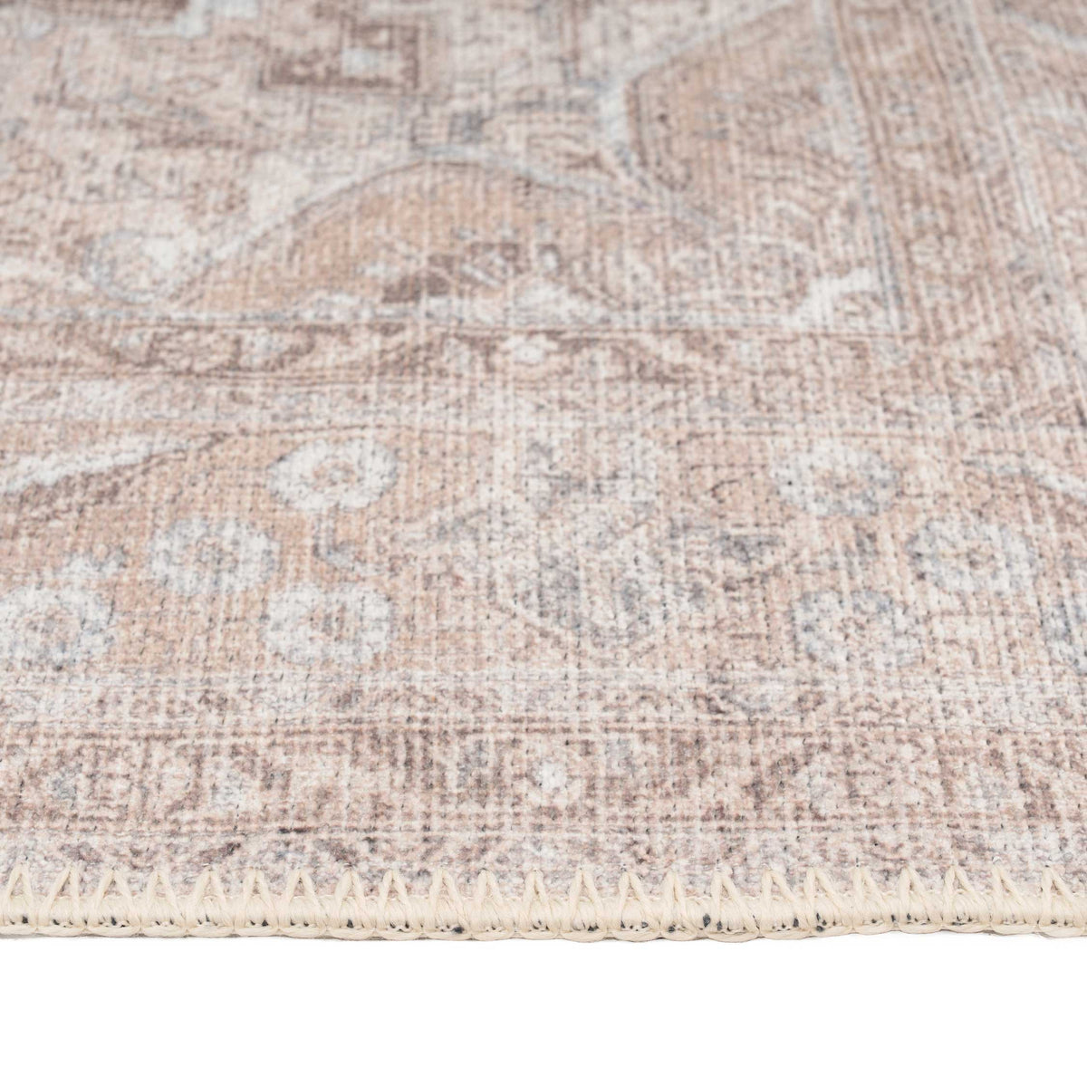 A close-up of a distressed traditional area rug with a faded beige, brown, and gray floral pattern, showing the woven texture and cream-colored fringed edge.