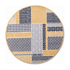 A round area rug featuring a patchwork design of geometric and floral patterns in mustard yellow, gray, and white, with a thin gold-toned border, shown on a plain white background.