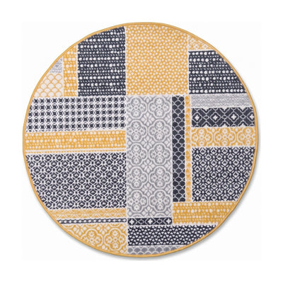 A round area rug featuring a patchwork design of geometric and floral patterns in mustard yellow, gray, and white, with a thin gold-toned border, shown on a plain white background.