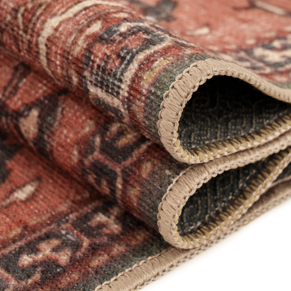 A close-up of a folded vintage-style area rug showing its intricate multicolor pattern and beige braided edges on a white background.