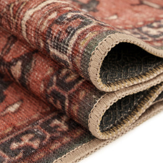 A close-up of a folded vintage-style area rug showing its intricate multicolor pattern and beige braided edges on a white background.