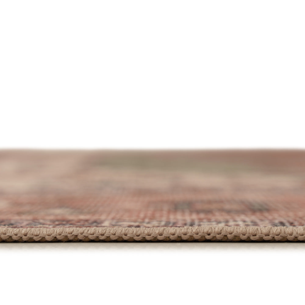 Close-up of a woven rug or textile edge showing a beige looped border and a soft, blurred multicolor pattern in warm earthy tones above a white background.