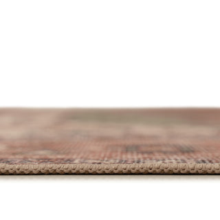 Close-up of a woven rug or textile edge showing a beige looped border and a soft, blurred multicolor pattern in warm earthy tones above a white background.