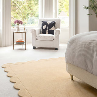 Modern bedroom with a white armchair, scalloped beige rug, and a bed.