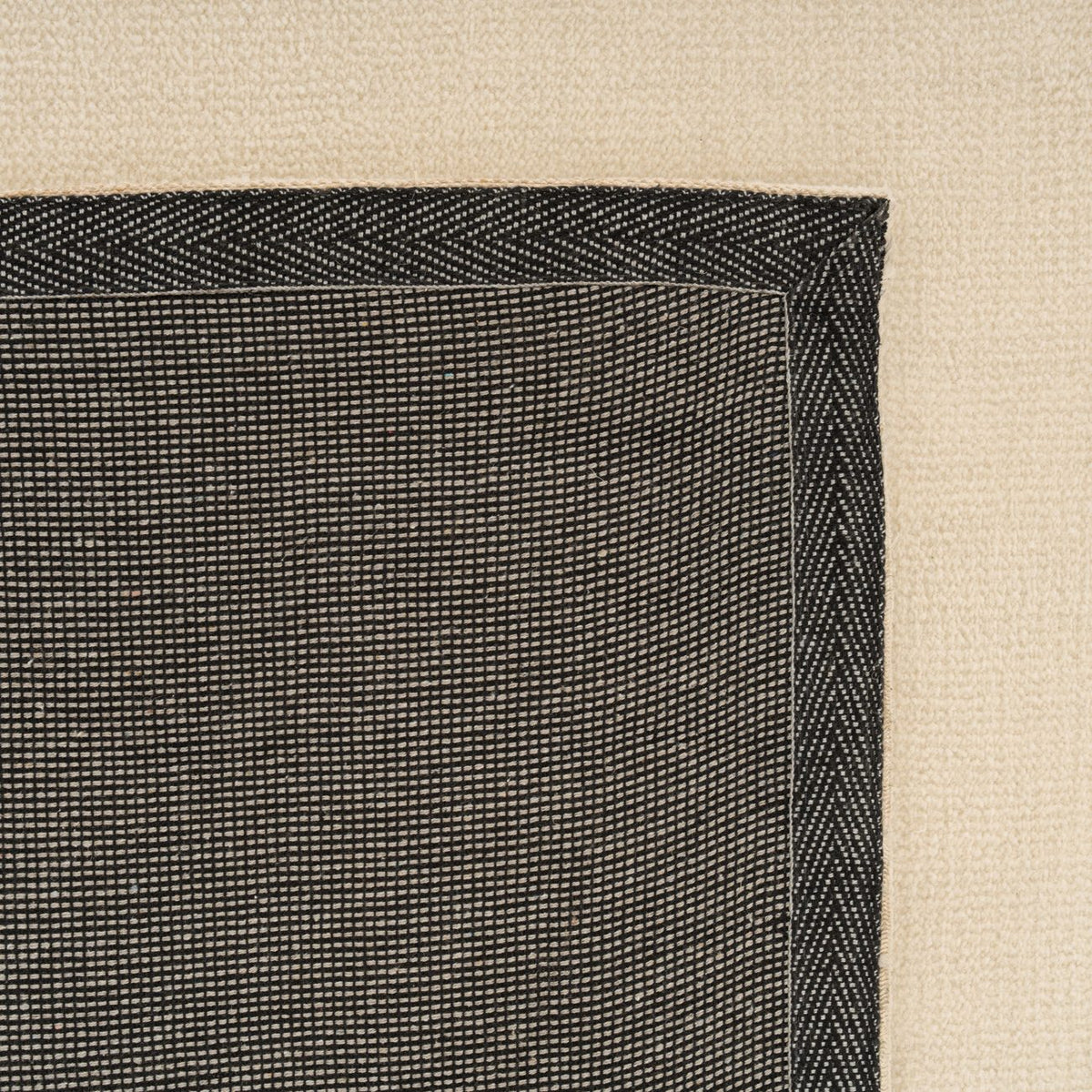 Close-up of a black textured rug corner on a beige background