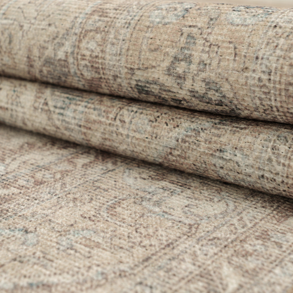 A close-up of a rolled area rug showing its distressed traditional pattern in beige, taupe, and muted gray tones.