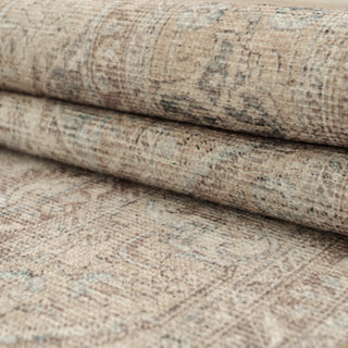 A close-up of a rolled area rug showing its distressed traditional pattern in beige, taupe, and muted gray tones.